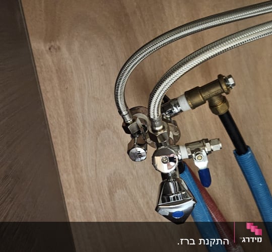 צינורות מים מתכתיים וברזים מתחת לכיור